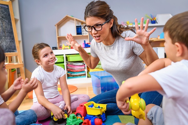 preschool teacher talking to group of children sitting on a floo